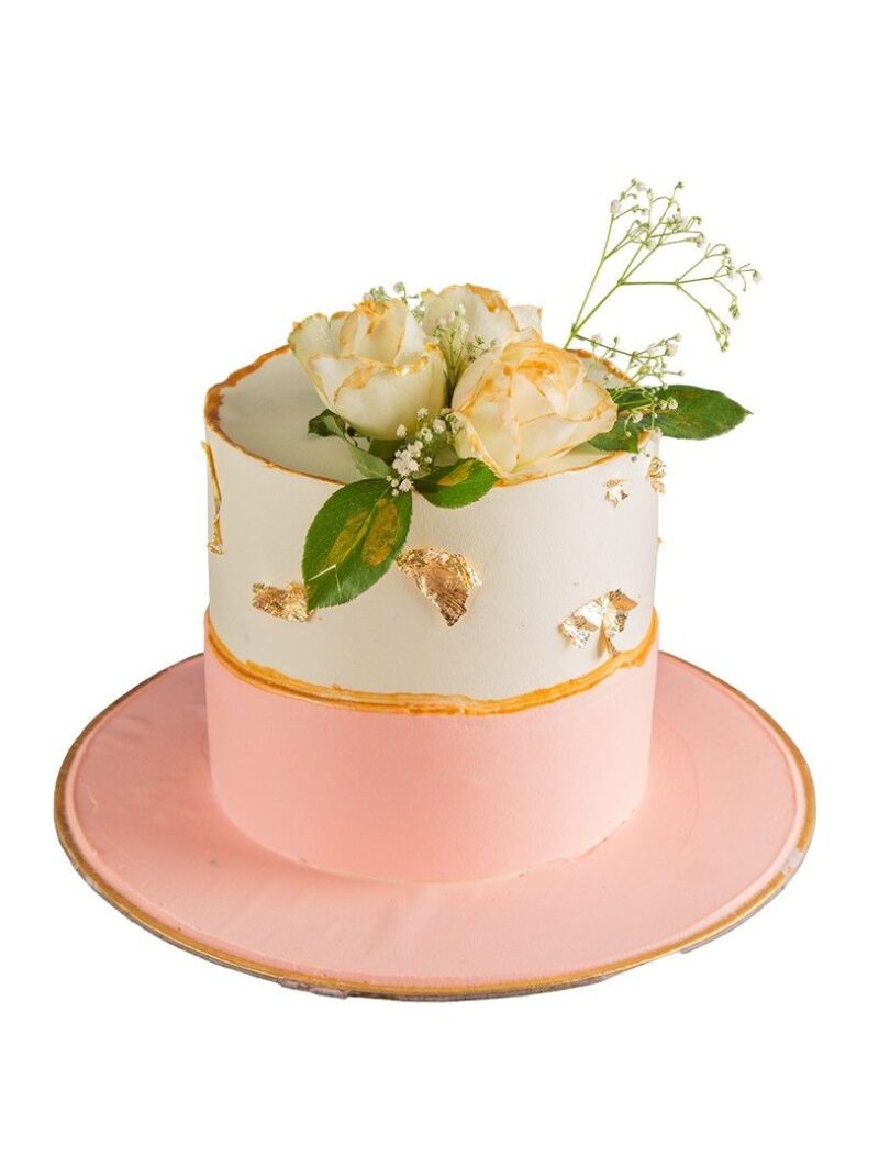 Elegant fresh floral cake with white and pink tiers, golden accents, and cream roses on top.
